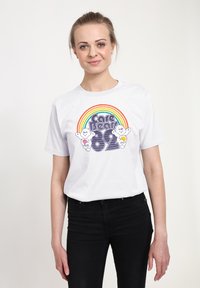Bílý bavlněný tričko s barevnou grafikou duhy a textem "Care Bears 82" spolu s ilustracemi kreslených medvídků. Krátké rukávy, kulatý výstřih.