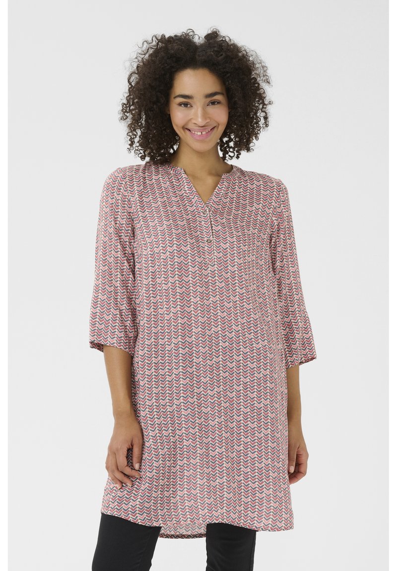 Tunique rouge et blanche avec un motif en zigzag, manches trois-quarts, décolleté en V et un détail de bouton au niveau du cou. Tissu doux, coupe décontractée.