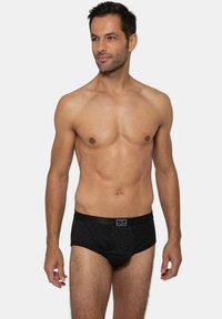 Slip da uomo a righe nere con un morbido elastico in vita che presenta una patch con il logo sulla parte anteriore. Il tessuto ha una consistenza liscia.