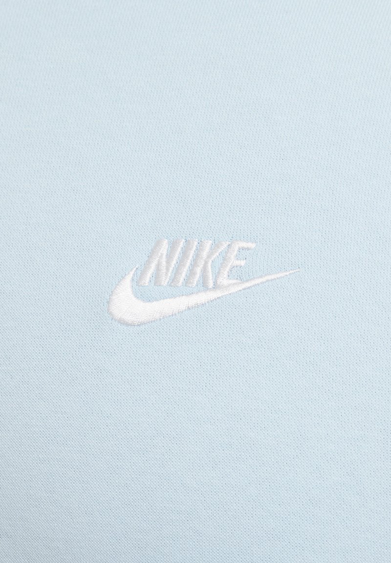 Tejido de algodón de color azul claro con un logo de Nike bordado en blanco, que presenta una textura suave y elementos de diseño sutiles.