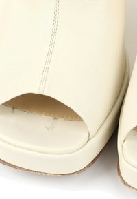 Gros plan de chaussures ouvertes en cuir couleur crème avec des coutures visibles et des semelles légèrement usées.