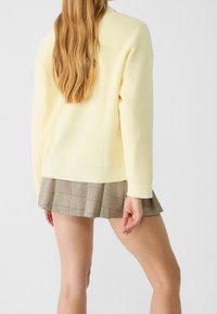 Jasnożółty sweter dziany o luźnym kroju i prążkowanej teksturze, zestawiony z plisowaną spódnicą w beżowo-brązową kratę.
