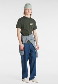 Mørk grøn bomulds t-shirt med Vans-logo, lys grå sweatshirt bundet om livet, løstsiddende mørkeblå jeans, hvide sneakers, og en mintfarvet beanie.