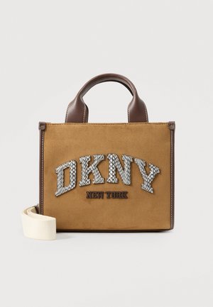 Sac cabas DKNY New York beige, avec des anses marron foncé, des lettres de logo à motifs et une bandoulière crème, sur un fond uni.
