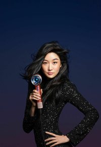 Dyson-hårfön, som har en snygg design med ett metalliskt rosa handtag, ett rundat luftutlopp och en sladd. Ytan har en texturerad finish.