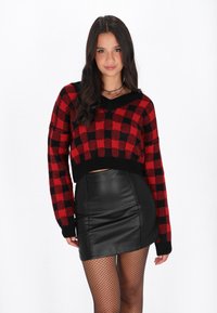 Maglione a maglia a scacchi rosso e nero con maniche lunghe e scollatura a V, abbinato a una mini gonna in pelle nera e collant a rete.