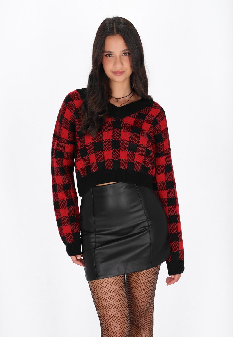Maglione a maglia a scacchi rosso e nero con maniche lunghe e scollatura a V, abbinato a una mini gonna in pelle nera e collant a rete.