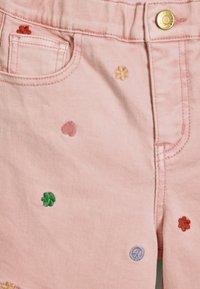 Roosa teksashortsid, millel on mitmevärviline lille- ja rahusümboli tikand, esi-tasku ja kuldne nööbiga detail.
