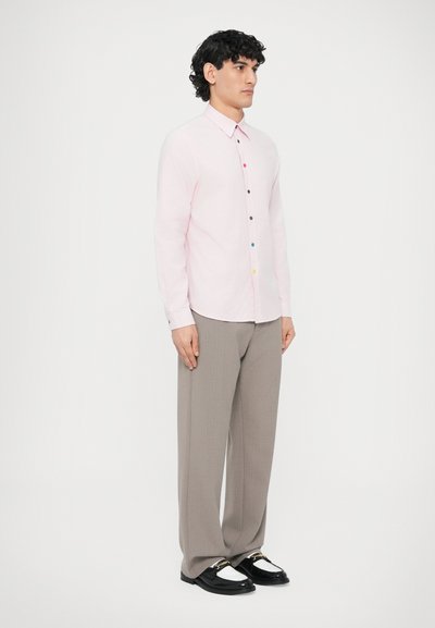 Cămașă roz deschis cu mâneci lungi, guler cu nasturi și nasturi multicolori, asortată cu pantaloni gri lejeri și pantofi negri.