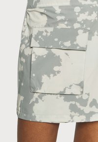 Falda gris claro con un patrón salpicado en blanco, con un gran bolsillo frontal y una tela suave y texturizada. El dobladillo es recto.