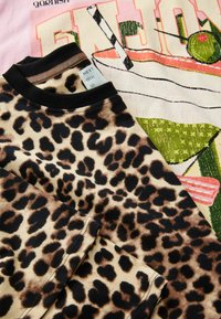 Leopard print fabric in shades of brown and black; features a black ribbed collar. Layered over a pink graphic T-shirt with colorful design.