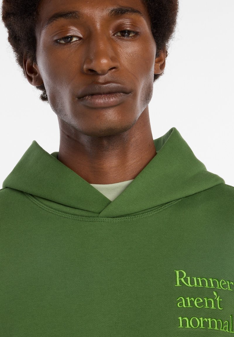Sweat-shirt vert à capuche, avec le texte « Runner's aren't normal » brodé en vert vif. Texture lisse, design décontracté.