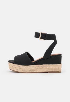 Black wedge sandal with an open toe and ankle strap, featuring a woven jute platform sole and a smooth upper material.