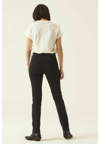 Jeans negros de tiro alto con una silueta ajustada, combinados con una camisa de manga corta de color claro. Tejido mate con estilo minimalista.