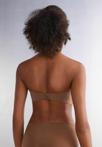 Tan podprsenka bez ramínek s hladkým povrchem a zapínáním na háček na zadní straně. Jednoduchý design, bez ozdob a s bezšvovým silhouette.