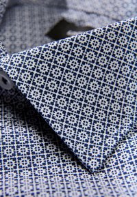 Overhemd met kraag, met een marineblauw geometrisch patroon op een witte achtergrond, gemaakt van lichtgewicht stof met een gladde textuur.