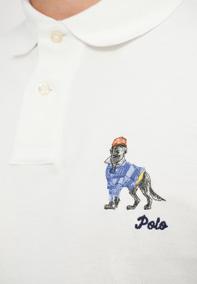 Camisa polo branca com três botões, apresentando um bordado detalhado de um cão usando um suéter azul e um chapéu vermelho, rotulada "Polo."