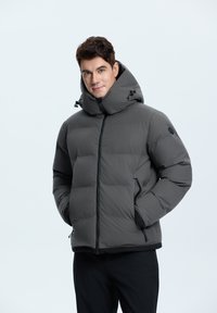 Dunkelgraue Pufferjacke mit hohem Kragen, Frontalreißverschluss, Seitentaschen, elastischen Bündchen und glatter Textur. Mit Kordelzügen an der Kapuze.