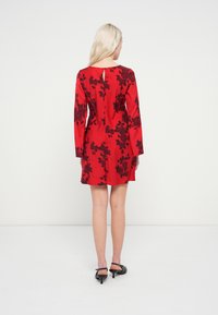 Rdeča obleka z dolgimi rokavi, okrašena s črnimi cvetličnimi vzorci. Na hrbtni strani ima ključavnico in je izdelana iz gladkega blaga. Oblečene so črne pete.