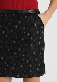 Falda negra con un diseño de estampado de leopardo en tonos grises y topo. Cuenta con una cintura de cuero sintético negro suave y bolsillos laterales.