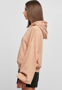 Pehmeast, heledast roosast kangast kapuutsiga sviiter. Omab ülevõetud varrukaid ja reguleeritavat kapuutsi. Kombineeritud mustade lühikeste pükstega vöökohtadest.