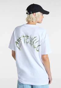 Witte katoenen t-shirt met een grote groene doornachtige graphic op de achterkant. Relaxed fit met korte mouwen en een ronde hals.