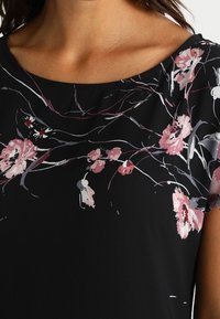 Top negro con estampado floral en tonos rosa, blanco y gris. Textura suave con cuello redondo y manga corta. Diseño sutil y elegante.
