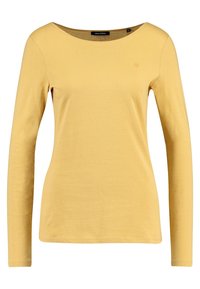 Keltainen pitkähihainen naisten paita, jossa on pyöreä kaula-aukko, vartalonmyötäinen leikkaus ja pieni brodeerattu logo vasemmassa rinnassa.