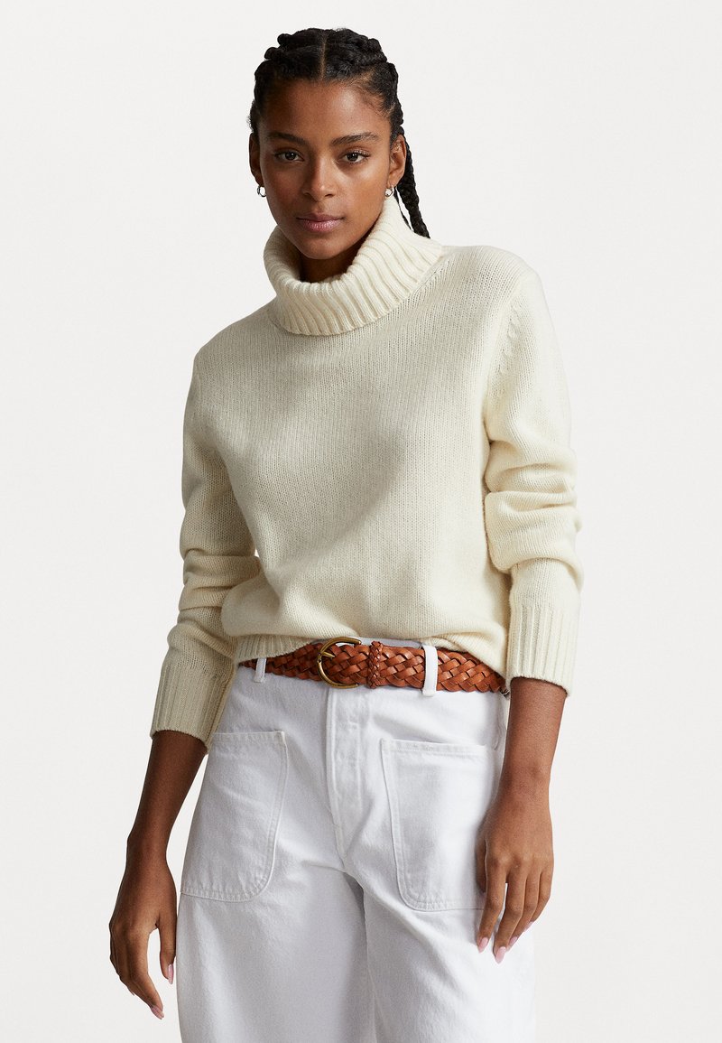 Cream-colored knit sweater with a ribbed turtleneck, paired with a braided brown belt and white high-waisted pants. Texture appears soft.