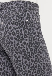 Sivé rifľové nohavice s čiernym leopardím vzorom, vybavené dvomi zadnými vreckami a striebornými kovovými súčiastkami na zapínanie.