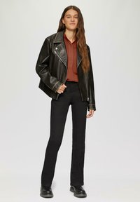 Czarna skórzana kurtka motocyklowa z srebrnym zamkiem, zestawiona z rdzawym koszulowym topem i czarnymi spódnicami w stylu dzwonów. Uzupełniona czarnymi butami.