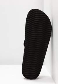 Černá gumová podrážka sandálů s vlnitou texturou, zaoblenou špičkou a výraznými okraji, která vykazuje jednoduchý design bez dalších ozdob.