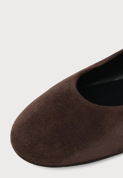 Gros plan d'une chaussure plate en daim marron avec un bout arrondi et une doublure intérieure noire sur un fond uni.