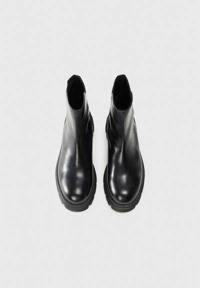 Botas de tobillo de cuero negro con un acabado suave, puntera redonda y suela de goma gruesa, con un diseño minimalista y sin herrajes visibles.