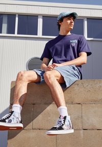 Marine kortærmet t-shirt med grønt Levi's-logo, lyseblå shorts og sorte højhalsede sneakers med fotoprint og hvide snørebånd.