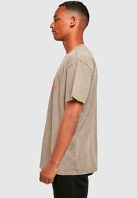 Graues, übergroßes T-Shirt mit pinkem Wolken-Graphic, aus weicher Baumwolle, mit kurzen Ärmeln und lockerer Passform. Seitenansicht.