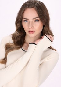 Maglietta a maniche lunghe color crema con bordino nero attorno al collo e ai polsi. Tessuto a costine e design aderente, che mette in mostra un tessuto morbido.