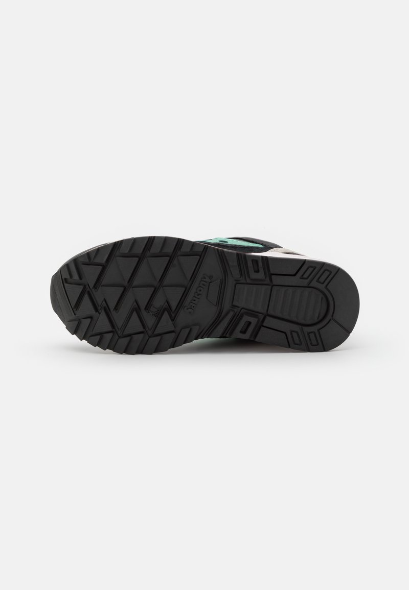 Schwarze Gummisohle eines Sneakers mit einem strukturierten Profil, das kantige Rillen aufweist, und einer soliden Mittelsohle in hellen Farben.