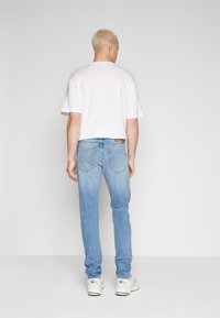 Lyse vaske denimjeans med slim fit, parret med en hvid t-shirt med rund hals. Skoene er hvide med sorte accenter.