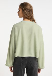 Maglione cropped di un verde chiaro, con texture a waffle, maniche lunghe e scollatura rotonda, abbinato a jeans scuri a vita alta.