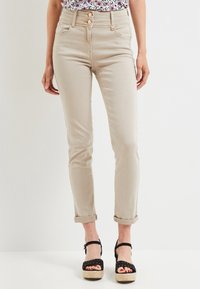 Jeans slim beige avec revers portés avec des sandales à plateaux noires et un haut à motifs, montrés de la taille aux pieds.