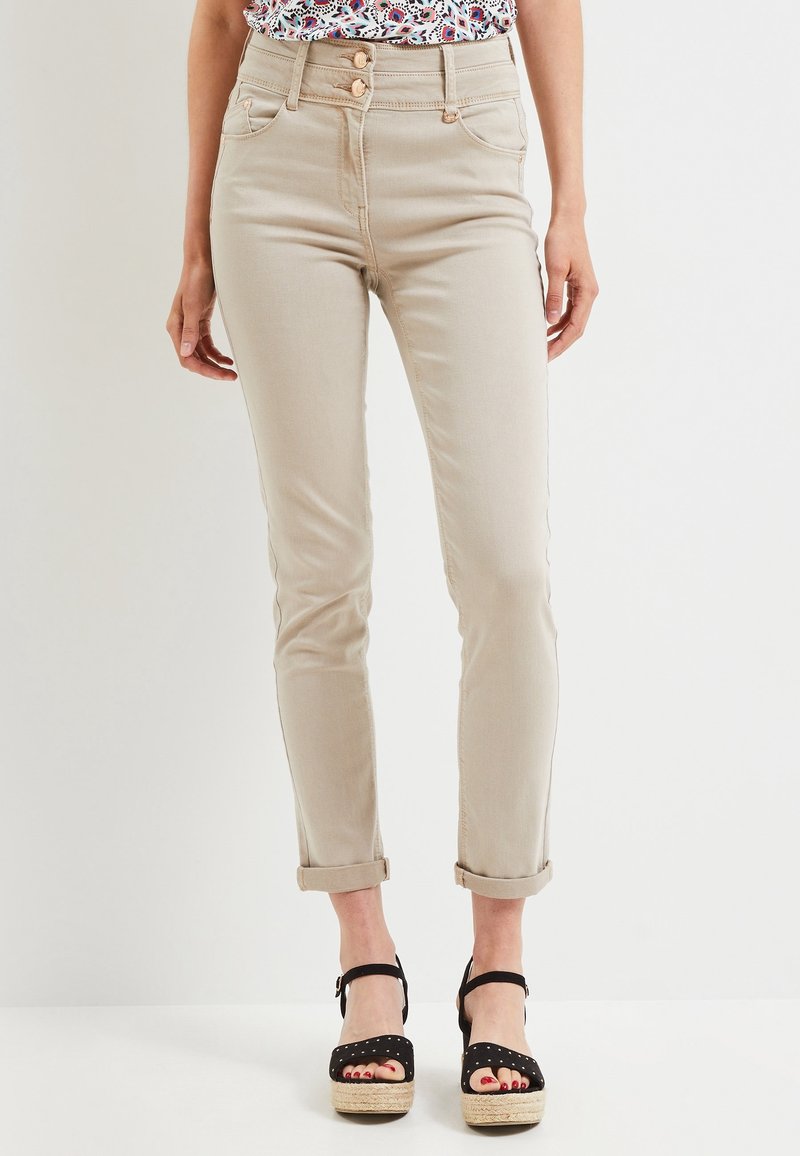 Jeans slim beige avec revers portés avec des sandales à plateaux noires et un haut à motifs, montrés de la taille aux pieds.