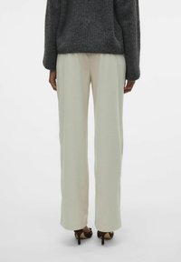 Lichtbeige, wijde broek met verticale ribbeltextuur. Hoge taille en een gladde afwerking, gecombineerd met een donkergrijze, oversized gebreide trui.
