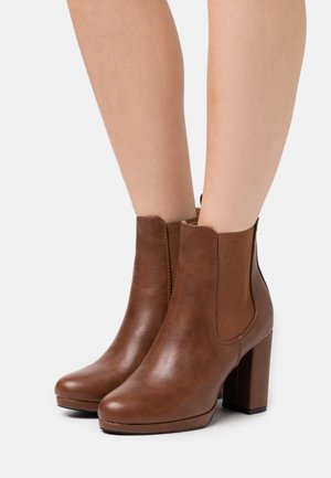 Botines de cuero marrón con tacón, que cuentan con paneles laterales elásticos, un acabado suave, punta redondeada y tacón grueso. Diseño duradero y ajustado.