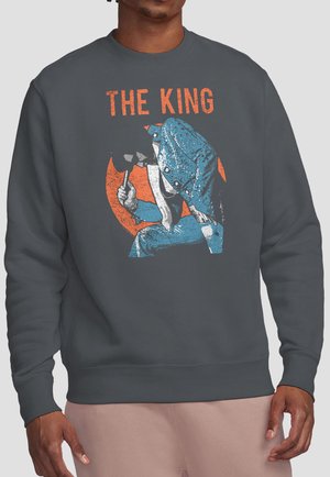 Man wearing dark gray sweatshirt with vintage-style graphic of a king in blue suit holding a hammer and text "THE KING" above it.