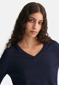 Maglione a maglia blu navy con scollo a V, maniche lunghe e una texture morbida. Il design è semplice, senza motivi o accenti visibili.