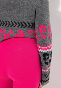 Harmaa neule, jossa on vaaleanpunaisia ja mustia leopardikuvioita, kuvioidut hihansuut ja vaaleanpunaiset legginsit. Materiaali näyttää pehmeältä, ja malli on tyköistuva.