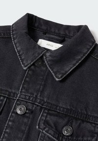 Svart jeansjacka med spetsig krage, två bröstfickor och svarta metallknappar. Tyget har en slät yta och subtila sömnadsdetaljer.