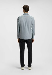 Hellblaues Langarmhemd mit Button-Down-Kragen, Rückenpasse und Manschetten. Kombiniert mit schwarzen Jeans und weißen Turnschuhen.