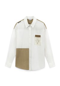 Weißes Hemd mit Knöpfen und beigen Teilen sowie einer Tasche mit einem Etikett. Das Design umfasst kontrastierende Schulterakzente. Aus Baumwollmaterial.